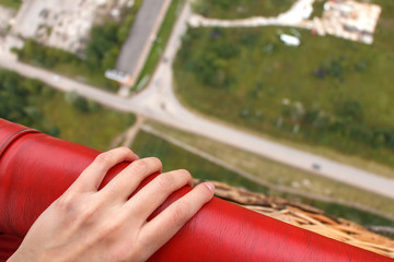 Women's hand holds the edge of the balloon basket. The view from a balloon basket down to the road...