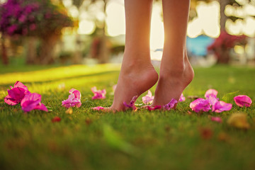 Close up female crossed legs walking on the grass,pink flowers on the grass