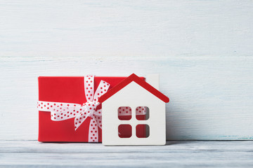 House model and gift box over white wooden background.