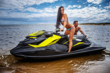 Attractive couple of a sexy girl and shirtless muscular male have fun with a jet ski on a seacoast.
