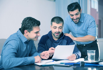 Three cheerful men reading documents at table