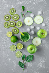 Healthy green smoothie with fresh green fruits and spinach leaves on gray background, top view