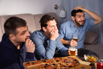 Worried concentrated men watching sporting match on tv with beer