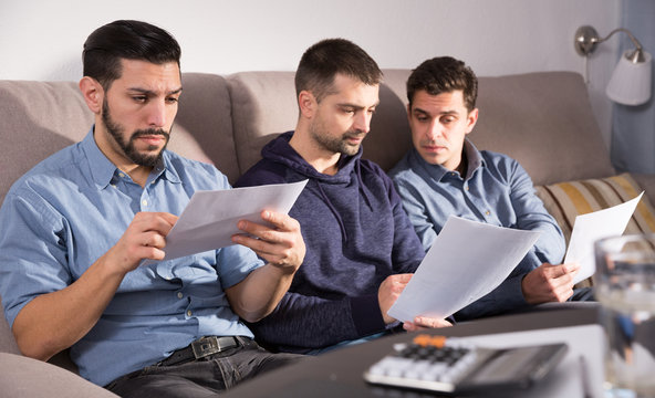 Three serious men discussing documents on sofa