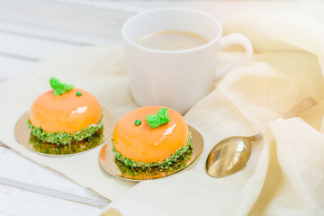 Bright orange mousse cakes and cup of coffee on white wooden tray
