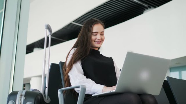 Airport Young female passenger on smart phone and laptop sitting in terminal hall while waiting for her flight, work businesswoman business notebook terminal, woman travel railway bus station