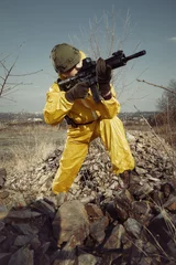 Tuinposter Freak gunman afraid of atomic war in yellow overall pointing noticeably on target © Couperfield
