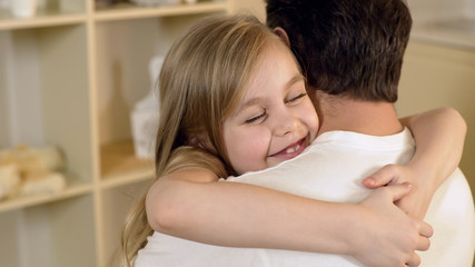 Beautiful little girl hugging father gently with happy smile on face, family
