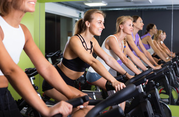 Fototapeta na wymiar Girls during workout on stationary bicycle in fitness gym