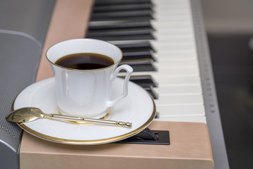 A cup of black coffee stands on the piano keys.