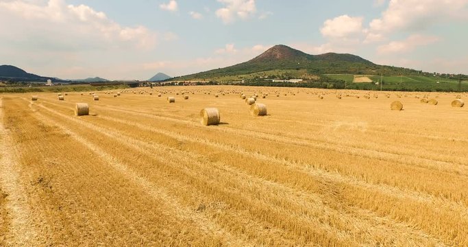 Aerial view of cropped wheat field with bales of hay in the countryside with a beautiful view of the mountain on a sunny day. Czech Republic