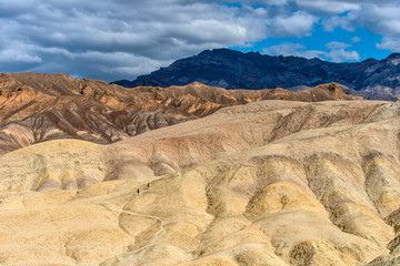 Hiking in Desert - Tourists hiking on steep and colorful rolling hills, as dark spring clouds passing overhead, in the Badlands of Death Valley National Park, California, USA.