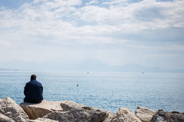 man seating and looking on the sea from stone pier. back view