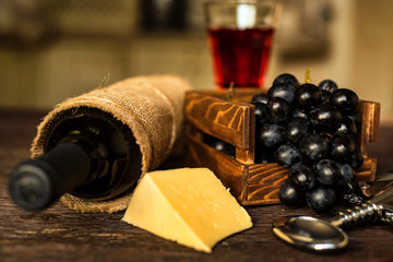 Glass of red wine with bottle, cheese and grapes