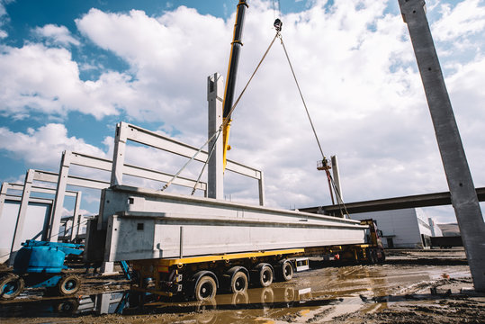 Industrial crane unloading prefabricated cement pillars from cargo
