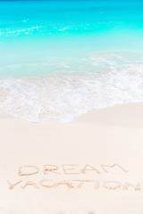 Fototapeta na wymiar Dream written on sandy beach with soft ocean wave on background
