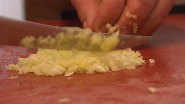 A medium shot of stove with a person chopping garlic