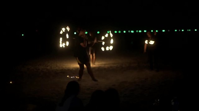 Few fire artists perform fire stunts on a beach in slow motion Light glare and visual tricks by spinning their torches in the air and on their bodies as they move around dark night on a sandy beach