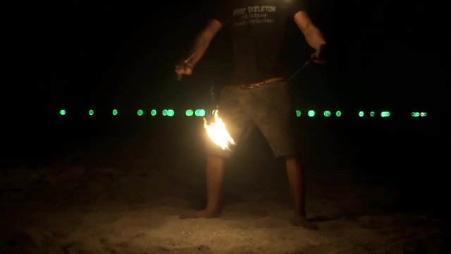 Close up fire artist performs  fire stunts on a beach in slow motion Light glare and visual tricks by spinning his fire torch around his body dark night on a sandy beach