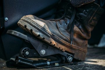 Fototapeta na wymiar Worker foot in large shoe or boot presses on pedal of industrial excavator or tractor