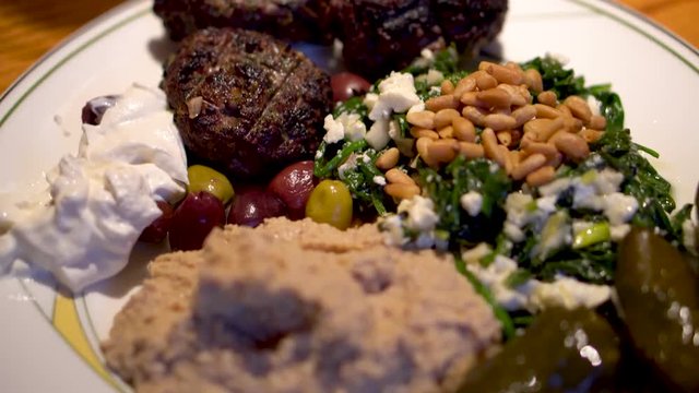 Closeup shot of middle eastern plate of kofta, hummus, spinach, olives, and grape leaves.