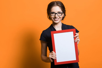 Portrait of confident beautiful young business woman holding frame in her hands standing on orange background