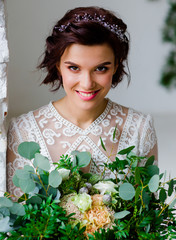A beautiful bride in a white room holds flowers in her hands