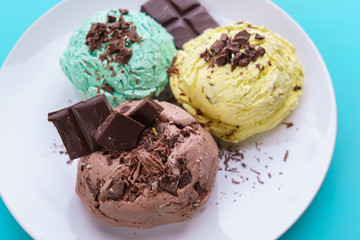 Mint, banana and chocolate ice cream scoops with chocolate crumbs served on white plate. Delicious refreshing summer sweets, close up