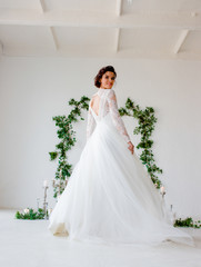 Amazing bride whirl in a white dress on a white background decorated with green leaves