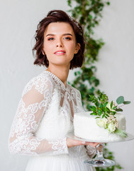 Elegant bride with short hair holds a wedding cake of white color in her hands