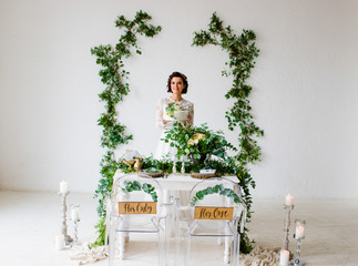 Happy wife standing near a decorated wedding arch holds a white cake