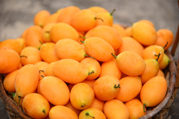 Sweet Marian Plum Plum Mango Gandaria in a bamboo basket on wooden table, concept of tropical fruits