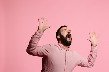 Screaming man with beard and both hands up in the air, mouth wide open, freaking out,  isolated on pink background