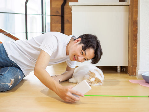 Handsome Chinese young man take selfie with a lazy fluffy cat at home.