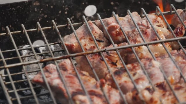 Grilling barbecue meat on wood coal. Man cooks appetizing hot shish kebab on metal skewers. Tasty meat pieces with crust. Grilling food. Closeup