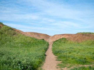 Path in grassy field leading to a dirt hill