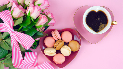 Obraz na płótnie Canvas Serving Mother's Day coffee and macarons with roses gift overhead on pink wood table background.