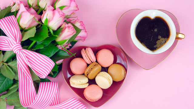 Serving Mother's Day coffee and macarons with roses gift overhead on pink wood table background.
