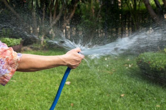 Woman holding rubber water hose watering garden