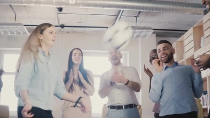Happy office employees hold a physical activity. Young multiethnic colleagues celebrating, playing with soccer ball 4K - Powered by Adobe