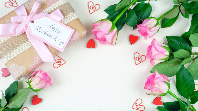 Happy Mother's Day overhead with gift and pink roses on white wood table background with copy space.