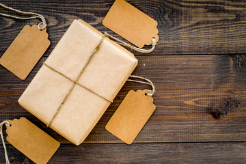 Parcel packaging box wrapped with craft paper with empty label mockup on dark wooden background top view copy space