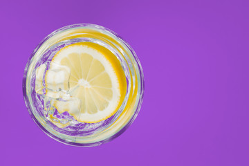Drink, water with lemon in a glass, on a purple background.
