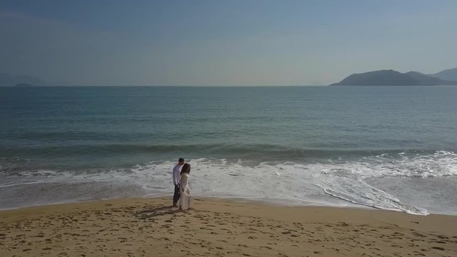 Newlyweds Walk on Wet Sand Beach against Ocean