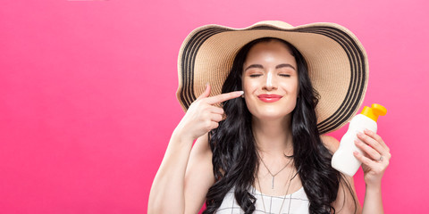 Young woman holding a bottle of sunblock on a solid background