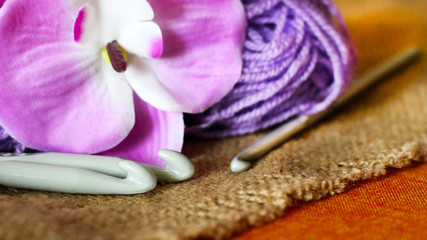 Fototapeta na wymiar Hooks for knitting, purple yarn, and a beautiful Orchid