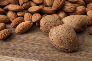 Mix of shelled and unshelled nuts with close up on an heap of almonds still in their shell with with almond kernel heaps in the background on a wooden rustic background