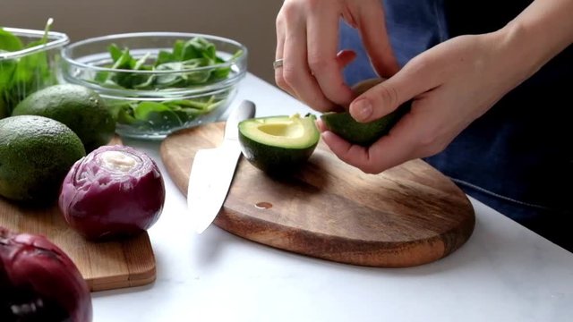 Woman Cutting Avocado and Peeling it with a Spoon