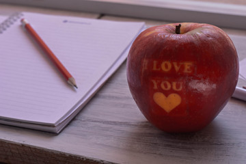 Fresh red apple with I love you sign whit a pen and open notebook at wooden background/ conceptual image of lunch break