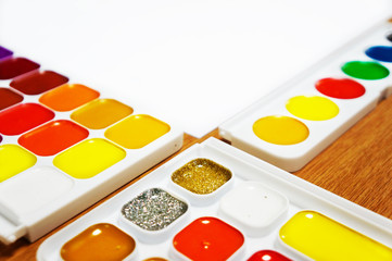 Set of watercolor paints and white blank paper, close up. Colorful artistic tools with empty space for text or sign